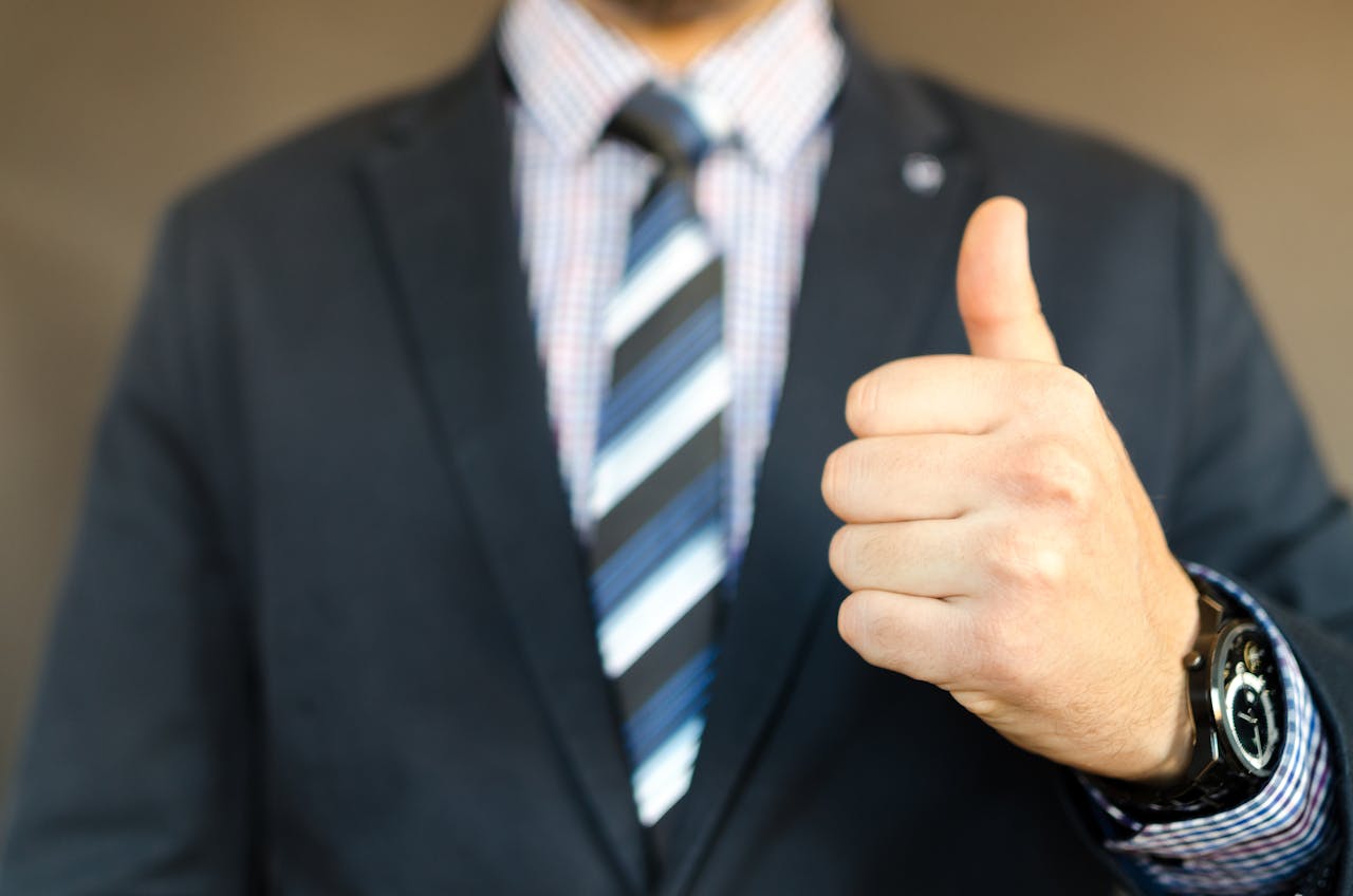 gallery-06 Close-up of a businessman in a suit giving a thumbs up gesture, symbolizing success.